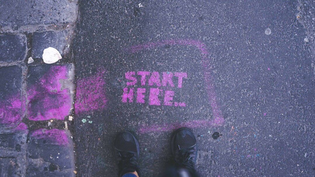 Photo of a graffiti stencil on a pavement which reads Start Here