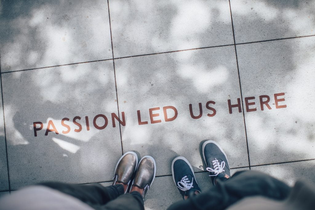 Photo of two people standing next to the words "Passion led us here" written on the pavement