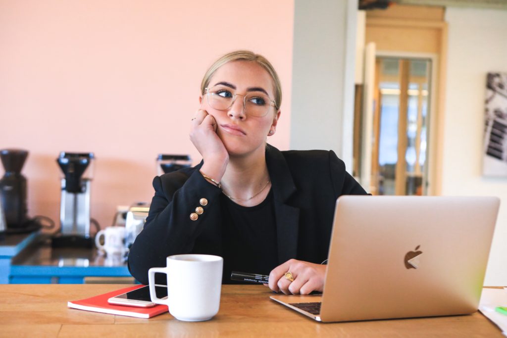 Photograph of a female employee sitting at her laptop ruminating and looking unhappy